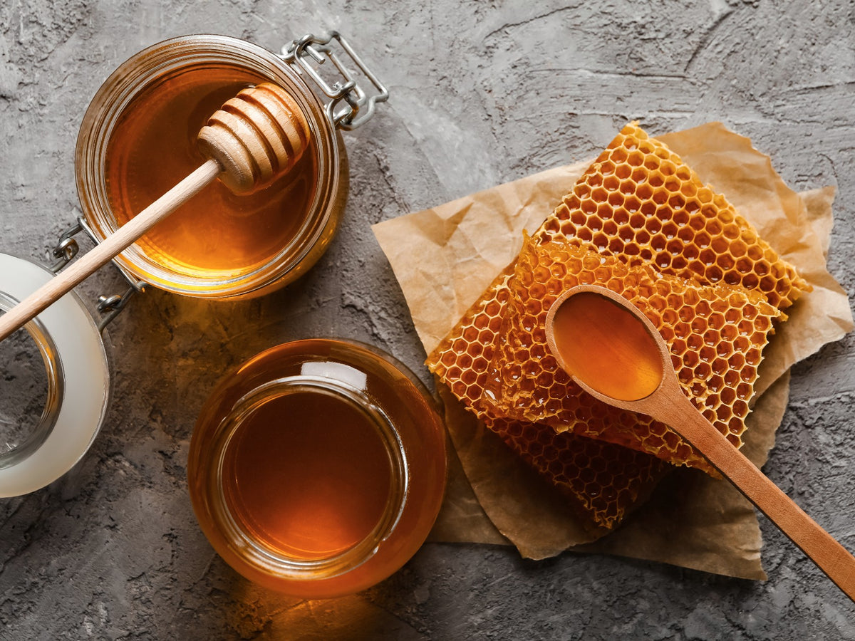 Two jars of honey with a honeycomb and dipper on a textured surface