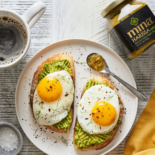 Avocado toast with eggs on a plate with a jar of harissa paste and a cup of coffee. The Spice & Tea Shoppe