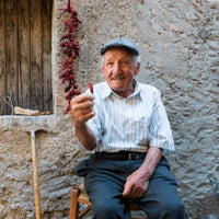 Older Italian man sits outside stone house with Calabrian chili peppers.