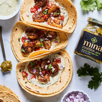 Tacos with chicken and vegetables on a white surface with a jar of harissa paste. The Spice & Tea Shoppe