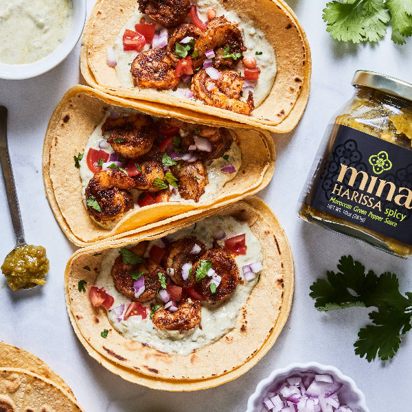 Tacos with chicken and vegetables on a white surface with a jar of harissa paste. The Spice & Tea Shoppe