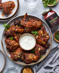 Platter of spicy wings with a dipping sauce, surrounded by a jar of harissa paste and garnishes. The Spice & Tea Shoppe