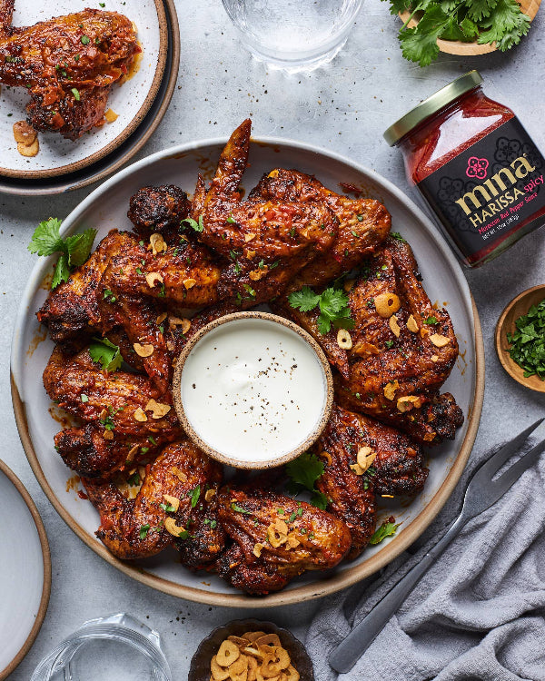 Platter of spicy wings with a dipping sauce, surrounded by a jar of harissa paste and garnishes. The Spice & Tea Shoppe