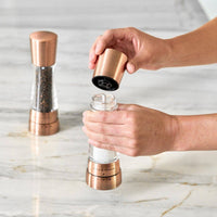 A pair of Cole & Mason Derwent salt and pepper mills in a metallic copper finish being filled.