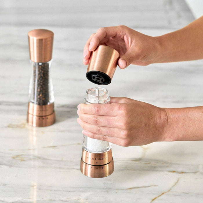 A pair of Cole & Mason Derwent salt and pepper mills in a metallic copper finish being filled.