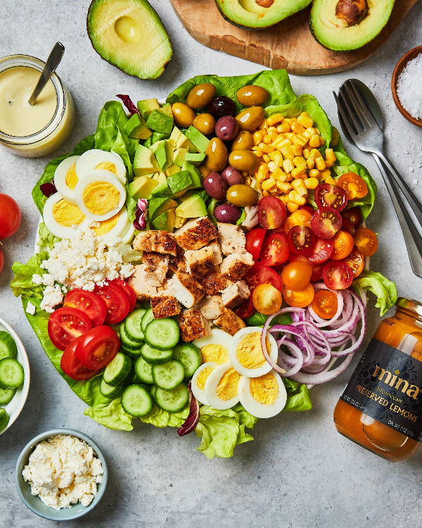 Colorful salad with various ingredients on a gray surface, including avocados, tomatoes, cucumbers, and eggs. The Spice & Tea Shoppe