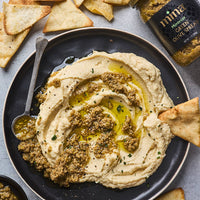 Hummus with olive tapenade on a plate with pita chips and a jar of olive oil.