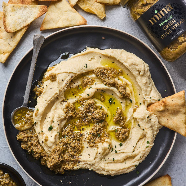 Hummus with olive tapenade on a plate with pita chips and a jar of olive oil.
