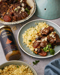 Plated dish of lamb tagine with couscous and a bottle of Mina Tagine sauce on a gray surface.  The Spice & Tea Shoppe