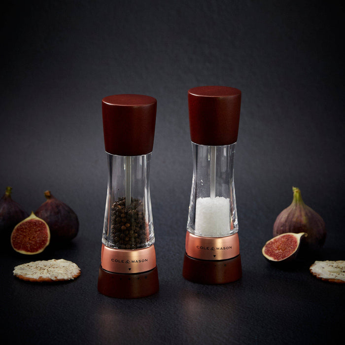 A pair of Cole & Mason Derwent salt and pepper mills featuring dark wood tops and bases with rose gold accents.