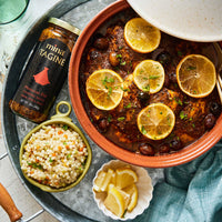 Casserole dish with lemon slices, jar of mina Tagine, and side dishes on a table. The spice & Tea Shoppe