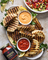Platter of grilled flatbread with dips and a jar of harissa sauce on a stone surface. The Spice & Tea Shoppe