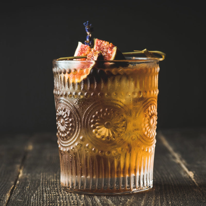 Bourbon and Fig Conserve Cocktail in cocktail glass on dark background, garnished with a fresh fig. The Spice & Tea Shoppe