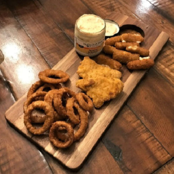 Assorted fried snacks on a wooden board with a jar of dipping sauce on a wooden table.