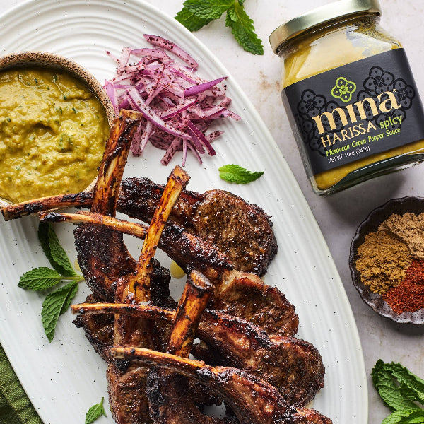 Plated dish of grilled lamb chops with a jar of Harissa spice and side dishes on a marble surface. The Spice & Tea Shoppe