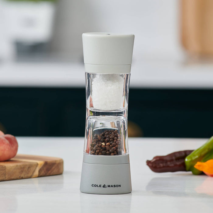 A Cole & Mason Lincoln Duo salt and pepper mill standing vertically on a dining table surrounded by plates of food.