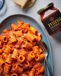 Pasta dish with a jar of Mina Harissa Hot Pepper Sauce on a gray surface. The Spice & Tea Shoppe