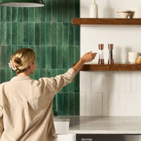 A woman reaching toward a pair of copper Cole & Mason salt and pepper mills on a wooden floating shelf in a modern kitchen.
