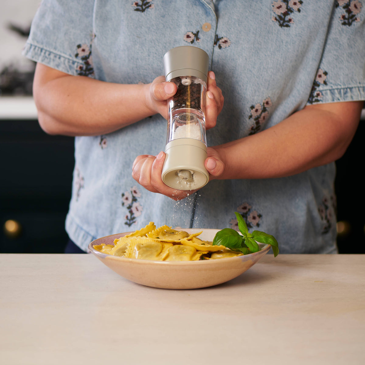 A Cole & Mason Lincoln Duo salt and pepper mill being used by a person to season their bowl of pasta.